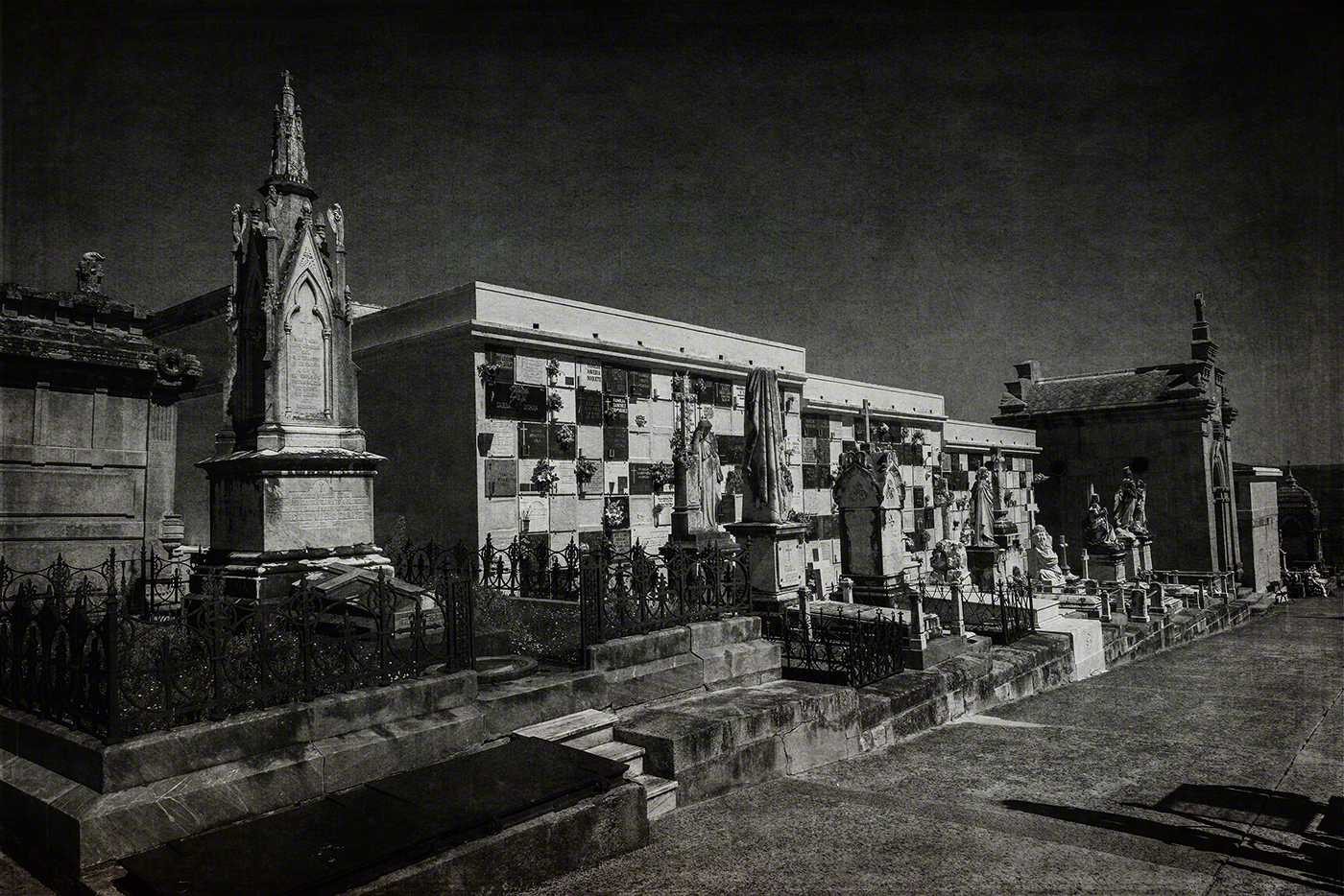 Black and white image of a cemetery with various tombstones, mausoleums, and statues, showcasing a somber atmosphere.