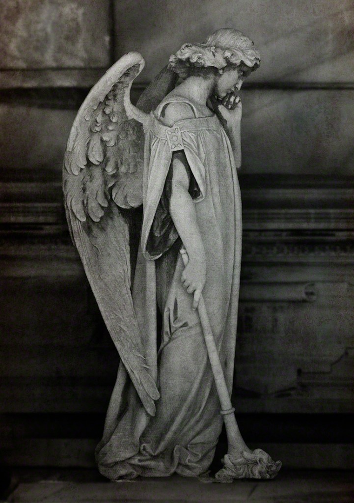 A solemn angel statue with large wings, holding a staff and gazing down thoughtfully, conveying a sense of reflection and sorrow.