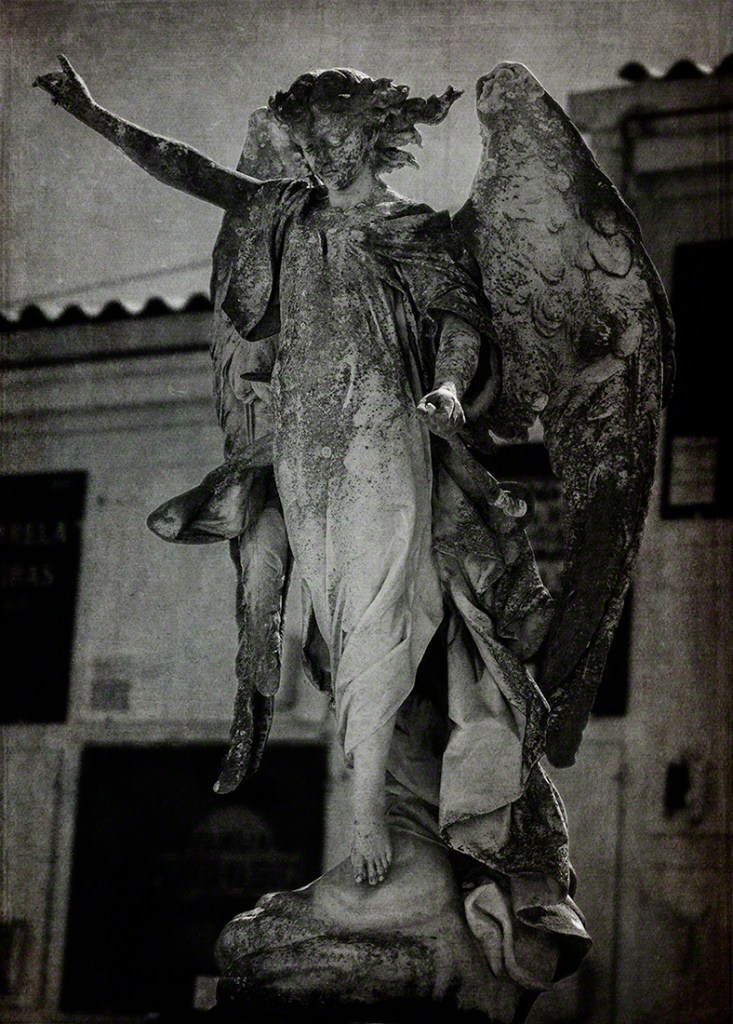 A weathered statue of an angel with outstretched arms, showcasing intricate details in a monochrome setting.
