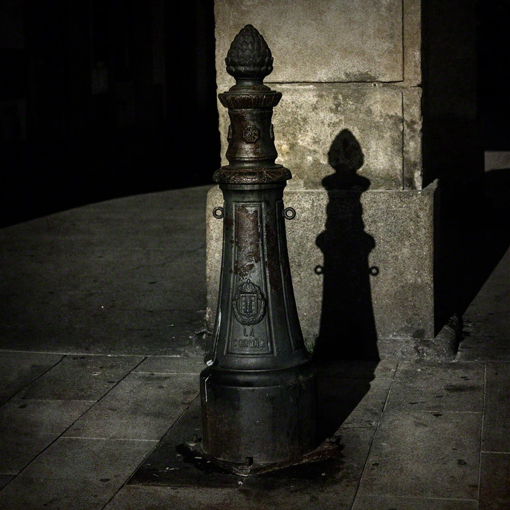 A vintage decorative streetlamp post with a prominent acorn-shaped top, casting a shadow on the ground in a dimly lit urban setting.